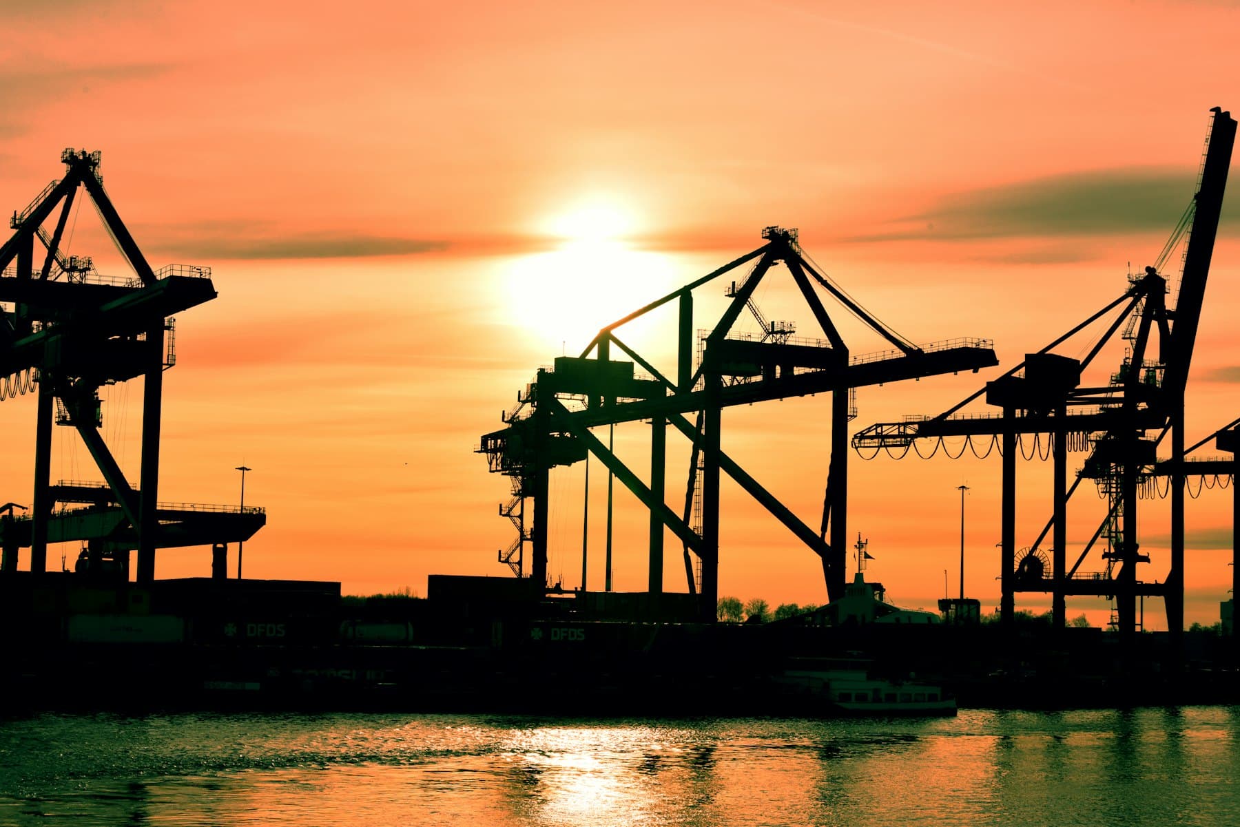 Puerto de exportación al atardecer con grúas y contenedores recortados contra un cielo dorado