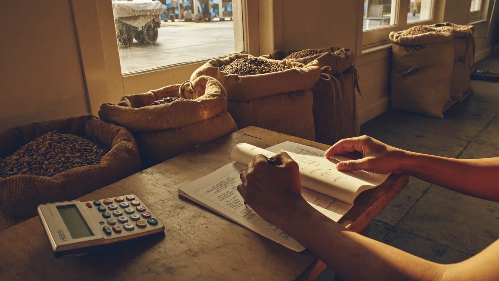 A food-business operator reviews the exchange figure on a ledger beside sacks of coffee and grain, before the currency change is made